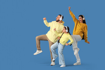 Happy parents with their little daughter in headphones dancing on blue background