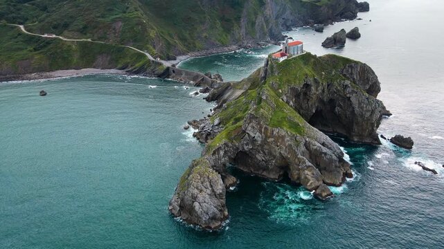 Aerial drone footage of San Juan de Gaztelugatxe, the iconic islet on the Basque coast of Spain. The video captures sweeping cinematic views of the winding stone bridge, the hermitage perched atop the