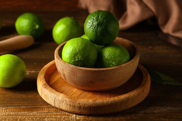 Bowl with fresh ripe limes on wooden background, closeup