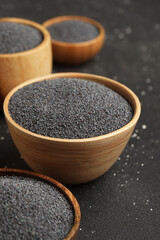 Wooden bowls with poppy seeds on black background, closeup