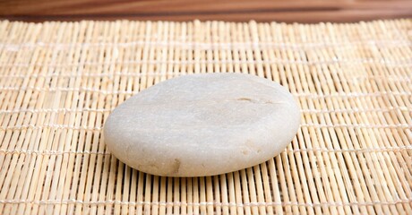 Smooth stone rests upon woven matting. Neutral tones dominate composition, creating calm visual experience. Simple, natural presentation.