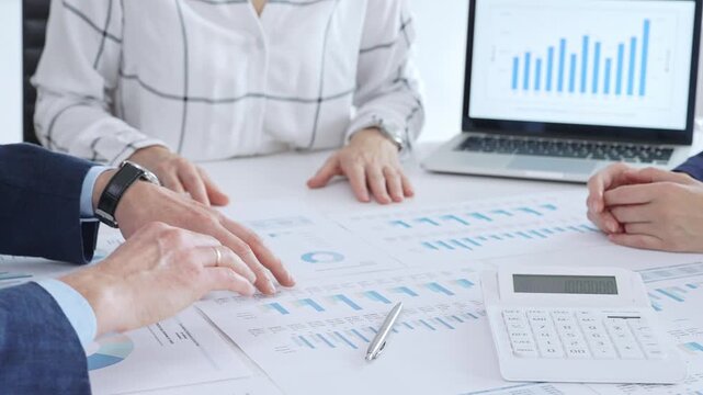 Business people professionals or accouters analyzing financial reports, charts and graphs on laptop and paper, using calculator to discuss strategy, budgeting and teamwork decisions