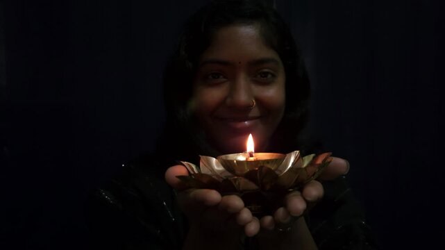 Beautiful Asian Indian girl holds a burning diya in her hands during the Diwali festival, celebrating Deepavali &mdash; the Hindu festival of lights &mdash; with a glowing traditional lamp in festive background.