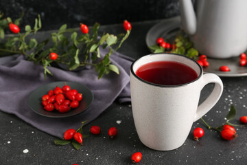 Cup of hot rose hip tea and berries on black background, closeup