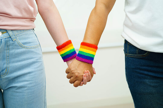 Asian LGBT couple woman holding hand wearing rainbow wristband.