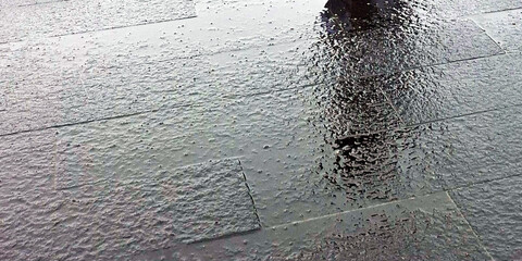 Reflection Of A Person Walking On A Wet Paved Surface During A Rainy Day