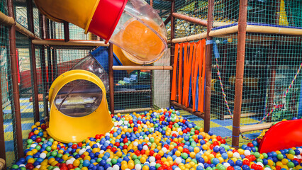 Colorful indoor playground with yellow transparent tube slide leading into bright ball pit filled with multicolored plastic balls, safe soft structures nets designed for children s active fun