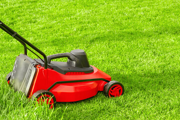 A red and black lawn mower stands on a green lawn.