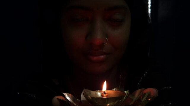Beautiful Asian Indian girl holds a burning diya in her hands during the Diwali festival, celebrating Deepavali &mdash; the Hindu festival of lights &mdash; with a glowing traditional lamp in festive background.
