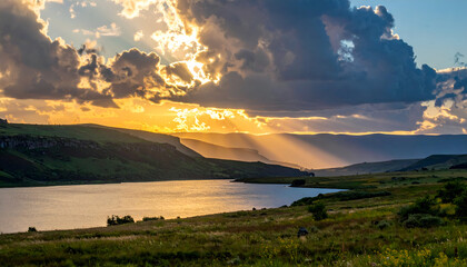 Scenic Golden Sunset at Mountain Lake with Dramatic Clouds and Reflections Over Water Landscape with Rolling Hills and Wildflowers in Foreground