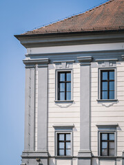 Close-up of a historic building facade in the old town of Cakovec, Croatia. Elegant architectural details and soft gray tones highlight the classic European design under a clear blue sky.