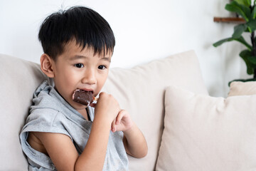 Asian boy enjoying a sweet chocolate ice cream, showing signs of sugar addiction and love for desserts. unhealthy eating habits, and the importance of balanced nutrition for children’s health.
