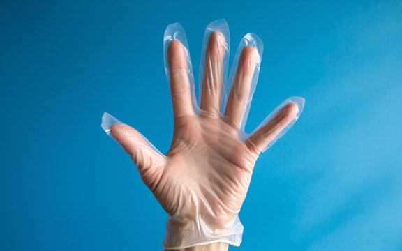 Hand wearing a disposable plastic glove against a vibrant blue backdrop - perfect for illustrating safety, hygiene, healthcare or food preparation concepts