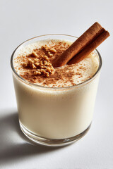 Eggnog drink with cinnamon stick and nutmeg topping in clear glass on white surface, creamy festive beverage
