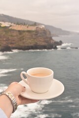 Morning coffee cup with ocean and rocky cliffs in the background. Peaceful coastal view, perfect for travel, relaxation, and lifestyle themes.