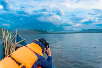 A tourist on a boat at Lake Muatanda in taking photos on a mobile phone, Kisoro Town, Uganda