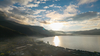 Fototapeta premium Villages by the Sunrise Lake and distant mountains, Lugu Lake in Sichuan, China
