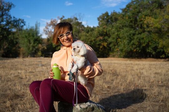 Senior Woman with maltese dog hydrating during outdoor activity