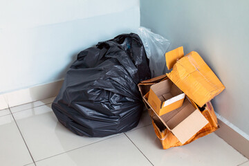 trash, waste, black garbage bag and cardboard boxes piled in the corner of an indoor room