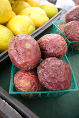The image shows a collection of passion fruits arranged on a black plastic crate with a grid pattern. The fruits vary in appearance—some are wrinkled and brownish