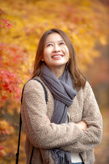 A cheerful woman wrapped in warm clothes stands amid vivid red and yellow maple leaves. Ideal for travel nature and seasonal content.
