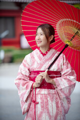 Smiling woman wearing traditional Japanese kimono and holding red umbrella in autumn park surrounded by colorful maple leaves. Perfect image for Japan culture and travel concept. Vertical image