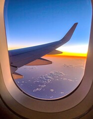 Airplane window view of vibrant sunset sky over clouds during flight.