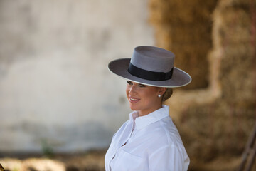 Portrait of a young, beautiful woman riding a horse, dressed in riding clothes and a typical Spanish hat.