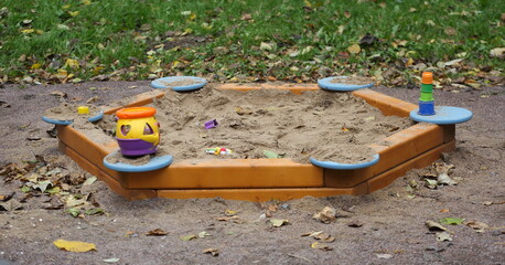 A children's sandbox at the edge of the playground near the lawn