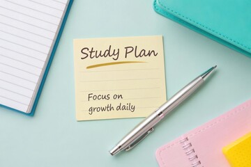 A sticky note with "Study Plan" rests on a blue surface near notebooks and a pen