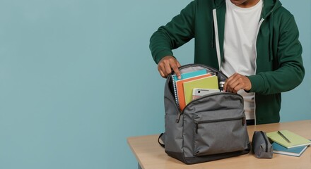 A young student packing his backpack with notebooks and school supplies on a desk. Preparing for college or a new semester. Back to school and education concept with copy space
