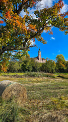 View of the Pilgrimage church Birnau in autumn day. Straw bale and tree with yellow red leaves in the foreground. Lake Constance, Baden-Wurttemberg, Germany.