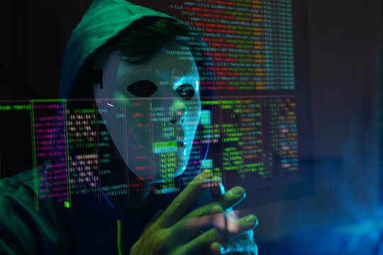 male hacker wearing a white mask sits in front of a screen, hands typing amid glowing cyber attack alerts and red binary code, symbolizing hacking, data breach, and malware in the night