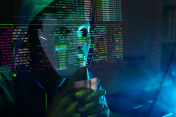 male hacker wearing a white mask sits in front of a screen, hands typing amid glowing cyber attack...