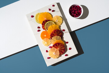 Rodajas de cítricos con semillas de granada en un plato de mármol blanco sobre fondo azul . Vista superior