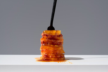 Rodajas de cítricos con caramelo líquido pinchadas con un tenedor sobre una mesa blanca y fondo...