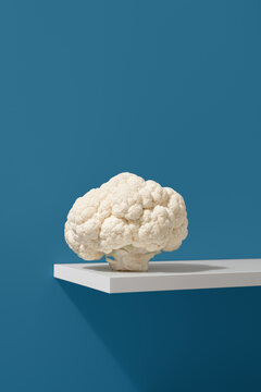Una coliflor fresca colocada sobre una estanter&iacute;a blanca y sobre un fondo azul.