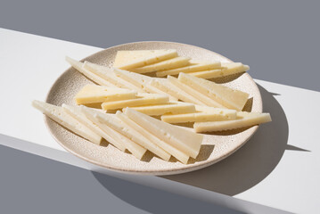 Trozos de queso de oveja curado y de cabra cortados en triángulos en un plato sobre fondo gris