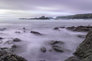 Ethereal Irish seascape with purple mist, jagged rocks, sea stacks, and distant cliffs at twilight.