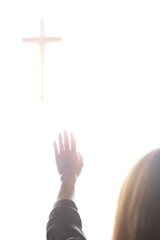 A Christian woman praying and worshipping with her hands raised toward the Holy Cross of Jesus Christ.
