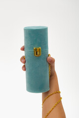 Closeup of a hand holding a blue velvet purse with gold clasp and chain; plush texture and elegant hardware create a luxurious accessory photo ideal for fashion.