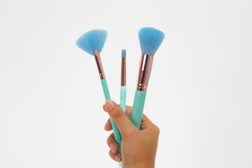 Closeup of a hand holding three makeup brushes one blue and two green showcasing varied bristle textures and colorful handles; beauty prop composition ideal for cosmetics branding.