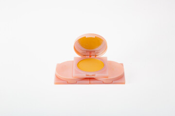 A small container of yellow powder is sitting on a white background. The container is pink and has a mirror on the lid. Concept of playfulness and fun.