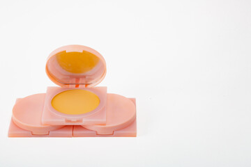 A small pink container with a yellow lid sits on a white background. The container is a makeup compact, and the yellow lid is a part of the makeup. Concept of simplicity and elegance.