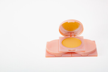 A pink and yellow makeup compact is sitting on a white background. The compact is made of plastic and has a mirror on top. Concept of beauty and elegance.