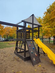 Wooden playground structure with slide and climbing wall in autumn  