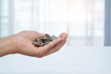 Man's hand holding a lot of coins and blurred window background. Money management and saving concept.