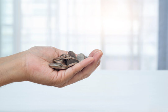 Man's hand holding a lot of coins and blurred window background. Money management and saving concept.