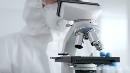 Close up of scientific researcher or virologist wearing protective gear is adjusting microscope, analyzing lab samples with precision in sterile research environment. Medicine and science concept