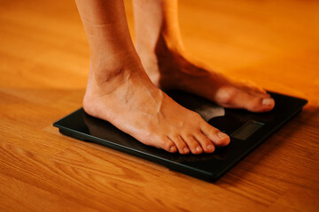 Person measures weight on a scale with bare feet on a wooden floor in the morning light